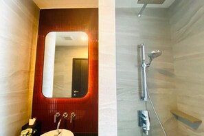 Une salle de bain avec un meuble-lavabo en bois, un miroir, un lavabo et une douche équipée d’un pommeau de douche à main.