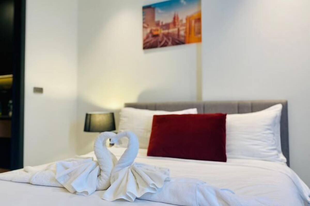 A hotel room with a bed, a red pillow, and a wall-mounted painting.