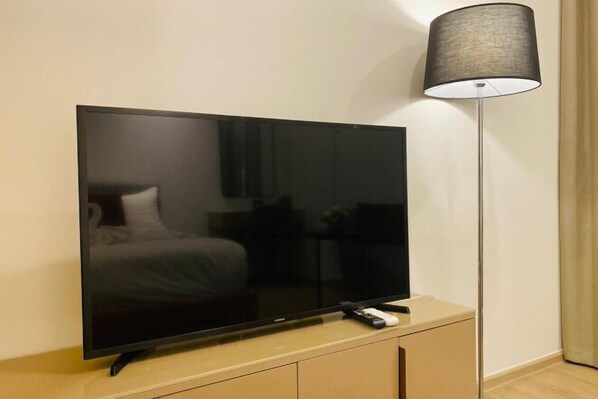 Un téléviseur à écran plat posé sur un meuble en bois, une télécommande et une lampe sur pied.