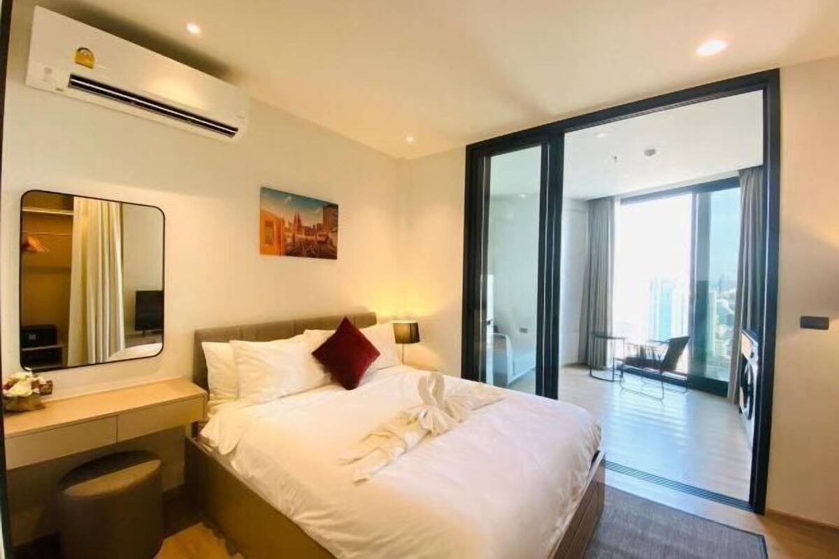 A hotel room with a bed, bedside table, mirror, and a view of the outside.