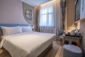 Et hotelværelse med en seng, et skrivebord, en stol og et rundt spejl.