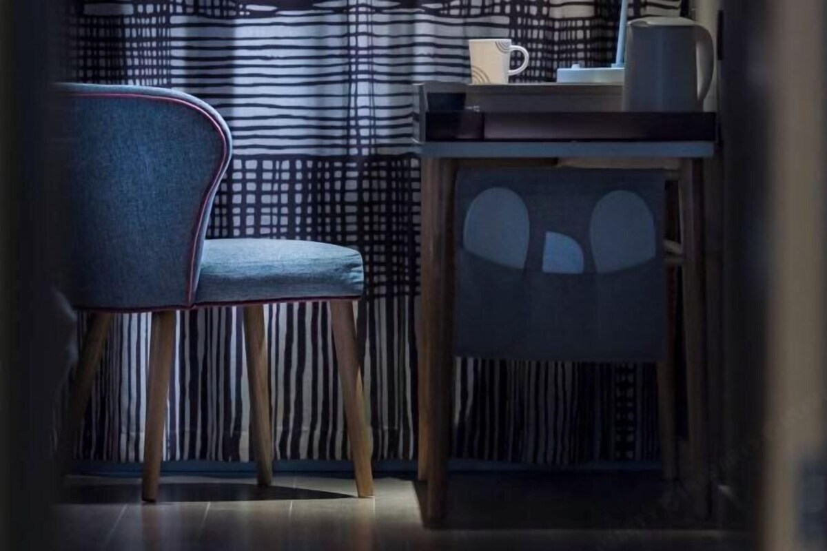 A corner of a room with a striped curtain, a chair, a table with a coffee pot, and a cup.