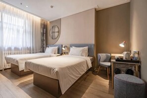 Et hotelværelse med to senge, et skrivebord med stol, en lampe og et lille bord.