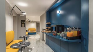 A modern dining area with a blue accent wall, a buffet counter with various food items, and yellow seating. - HOTEL XX SETTEMBRE (Rome)