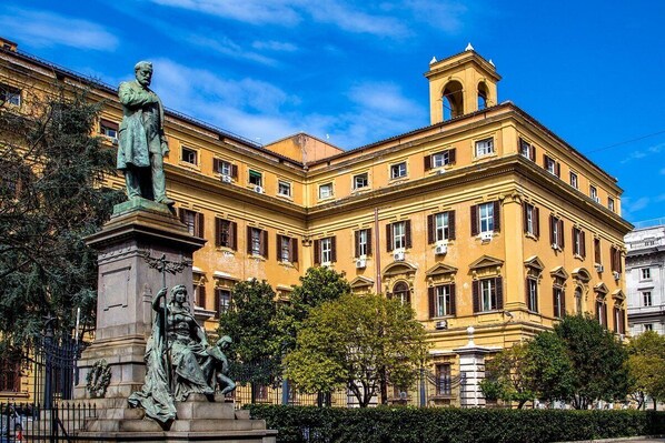 A historic building with classical architecture, featuring a prominent statue in front.