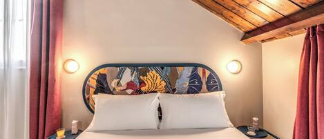 A hotel room with a bed, a nightstand, a bedside table, and a ceiling with exposed beams.