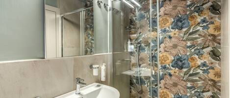 Un baño con lavamanos blanco, un espejo y una ducha con papel tapiz floral.