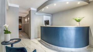 A modern reception area with a curved blue counter, marble flooring, and a small table with a vase of flowers. - HOTEL XX SETTEMBRE (Rome)