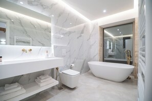 A modern bathroom with a large white bathtub, a white vanity with gold fixtures, and marble walls. - Fantasea Villas, villa Lux (Sternes)