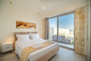 A bedroom with a large bed, a nightstand, a painting on the wall, and a view of the outside balcony. - Fantasea Villas, villa Lux (Sternes)
