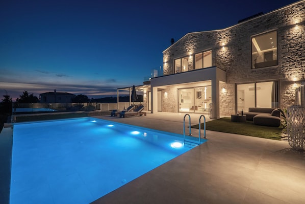 A modern house with a swimming pool, stone facade, and outdoor seating area.