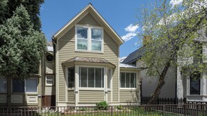 A two-story house with a gabled roof, a bay window, and a fenced yard with a tree and a small bush.