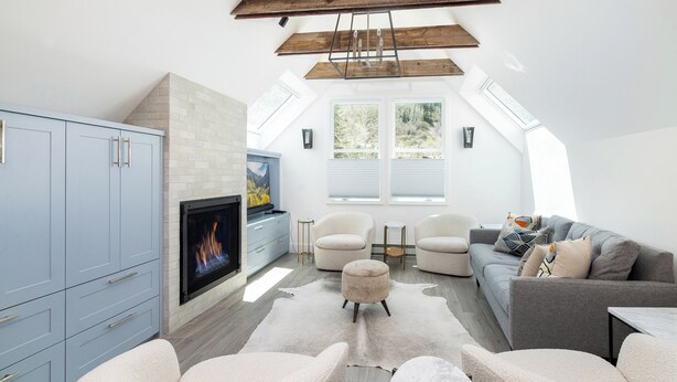 A modern loft with a fireplace, a grey sofa, a white armchair, and a large window providing natural light.