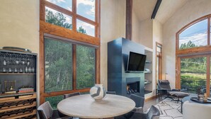 Un salon moderne avec une table ronde, des sièges confortables, une cheminée et de grandes fenêtres donnant sur l’extérieur.