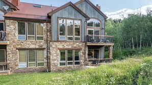 Une maison à deux étages, avec une façade en pierre et en bois, de grandes fenêtres et un balcon.