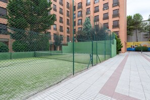 A tennis court enclosed by a green fence, with a tiled walkway in front. - GuestReady Essential - Relaxing stay in Barajas (Madrid)