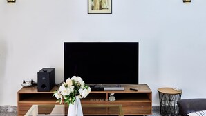 Un salon doté d’un grand téléviseur à écran plat, d’un meuble de rangement en bois, d’une petite table ronde et d’un tableau encadré accroché au mur.