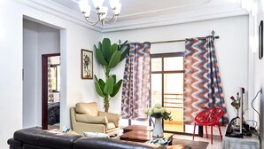 Un salon avec un canapé, un fauteuil, une plante, un vase de fleurs et un fauteuil rouge.