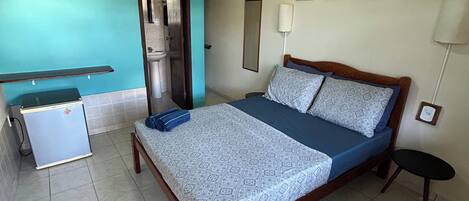 Ein Schlafzimmer mit Bett, Deckenventilator, kleinem Tisch, Stuhl, Wandlampe und einer Tür zum Badezimmer.