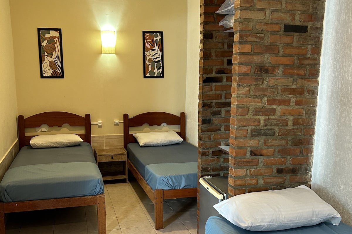 A room with two wooden beds, a brick partition, and a ceiling fan.