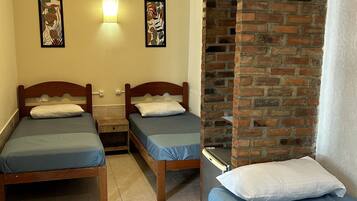 Una habitación con dos camas de madera, un separador de ladrillo y un ventilador de techo.