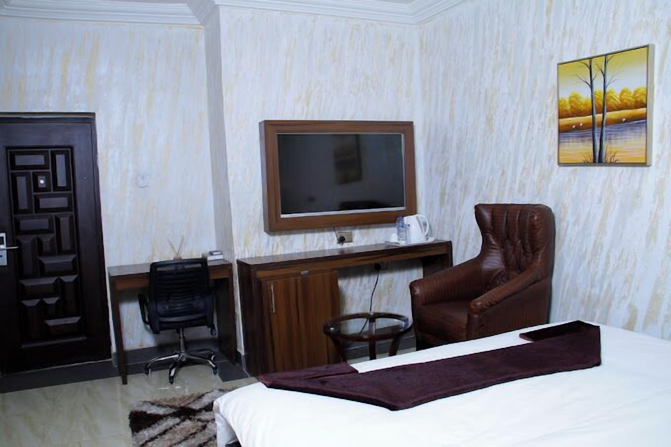 A hotel room with a bed, a desk, a chair, a television, and a painting on the wall.