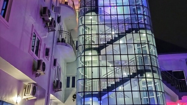Un hotel moderno con fachada de vidrio, varios balcones y una escalera visible.
