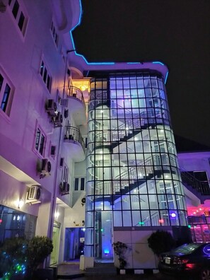 A modern hotel with a glass facade, multiple balconies, and a visible staircase. - Ugwis Hotel and Suites (Calabar)
