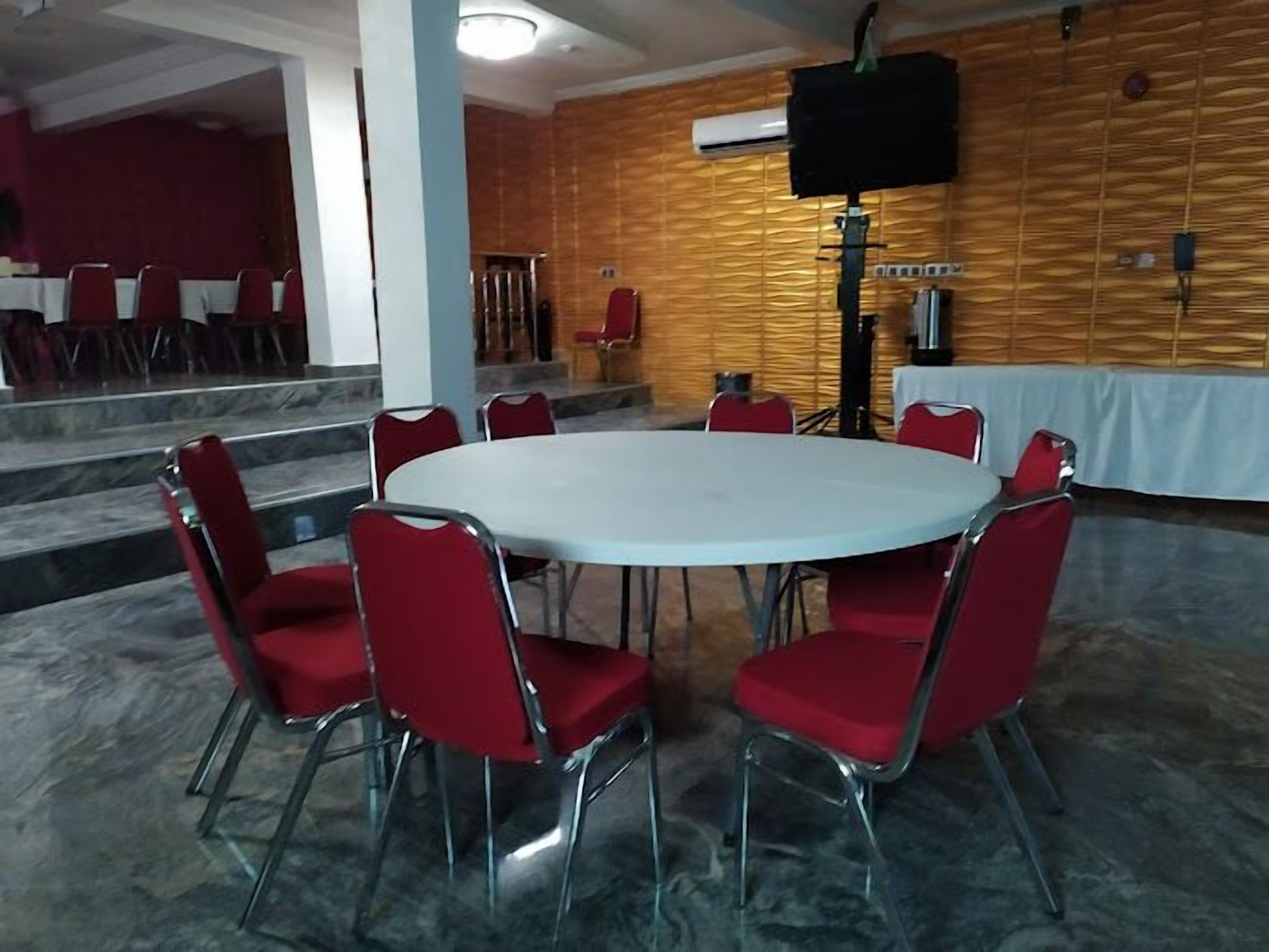 A conference room with a round table and red chairs, a wooden wall with a speaker, and a staircase leading to another room.
