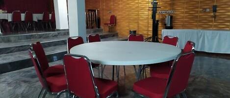 A conference room with a round table and red chairs, a wooden wall with a speaker, and a staircase leading to another room.