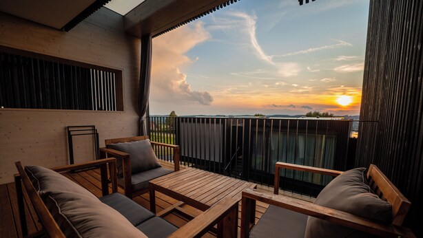 Una terraza de madera con una mesa y sillas, vista al atardecer y una barandilla.