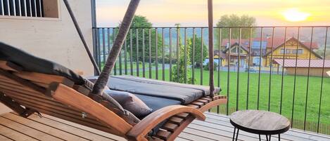 A wooden deck with a hammock, a small round table, and a view of a green landscape and houses in the background.