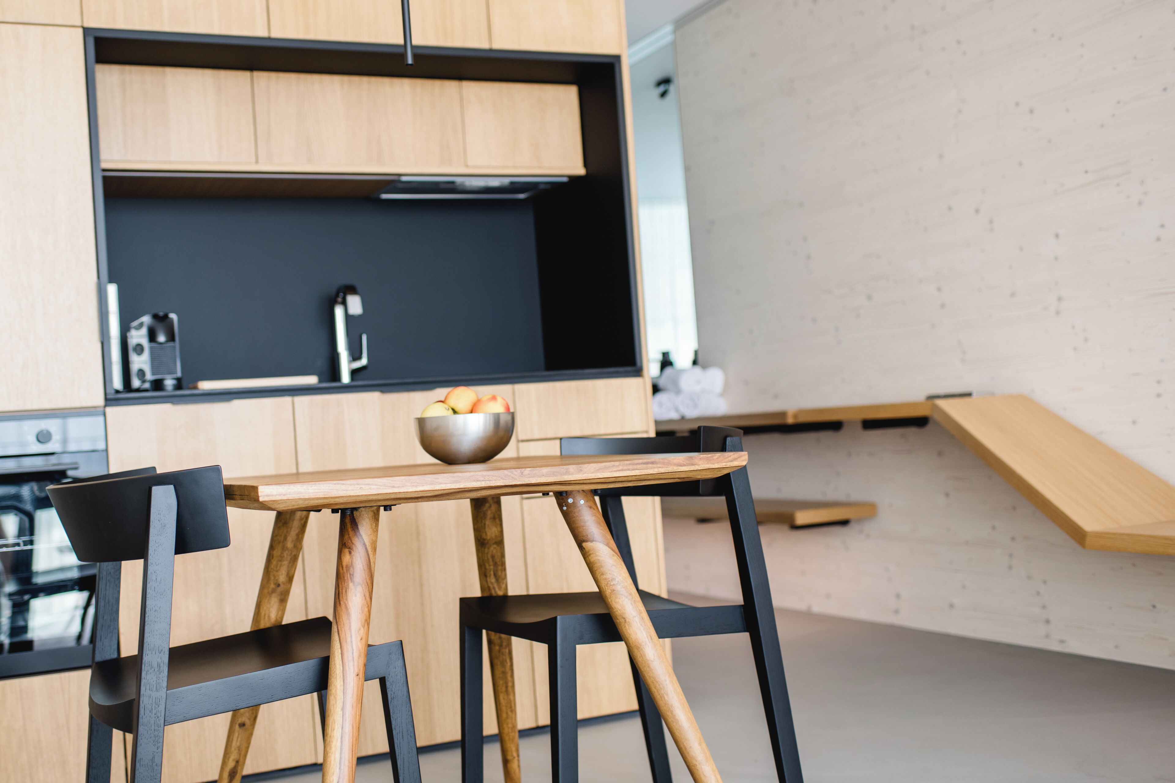 Una cocina moderna con armarios de madera, encimera negra y una mesa de madera con un tazón de fruta.