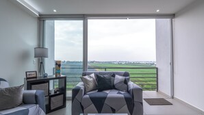 A modern living room with a sofa and armchair, a glass coffee table, and a view of a green landscape through large windows. - Modern Apartment with Terrace and Pool  (Tlajomulco de Zúñiga)