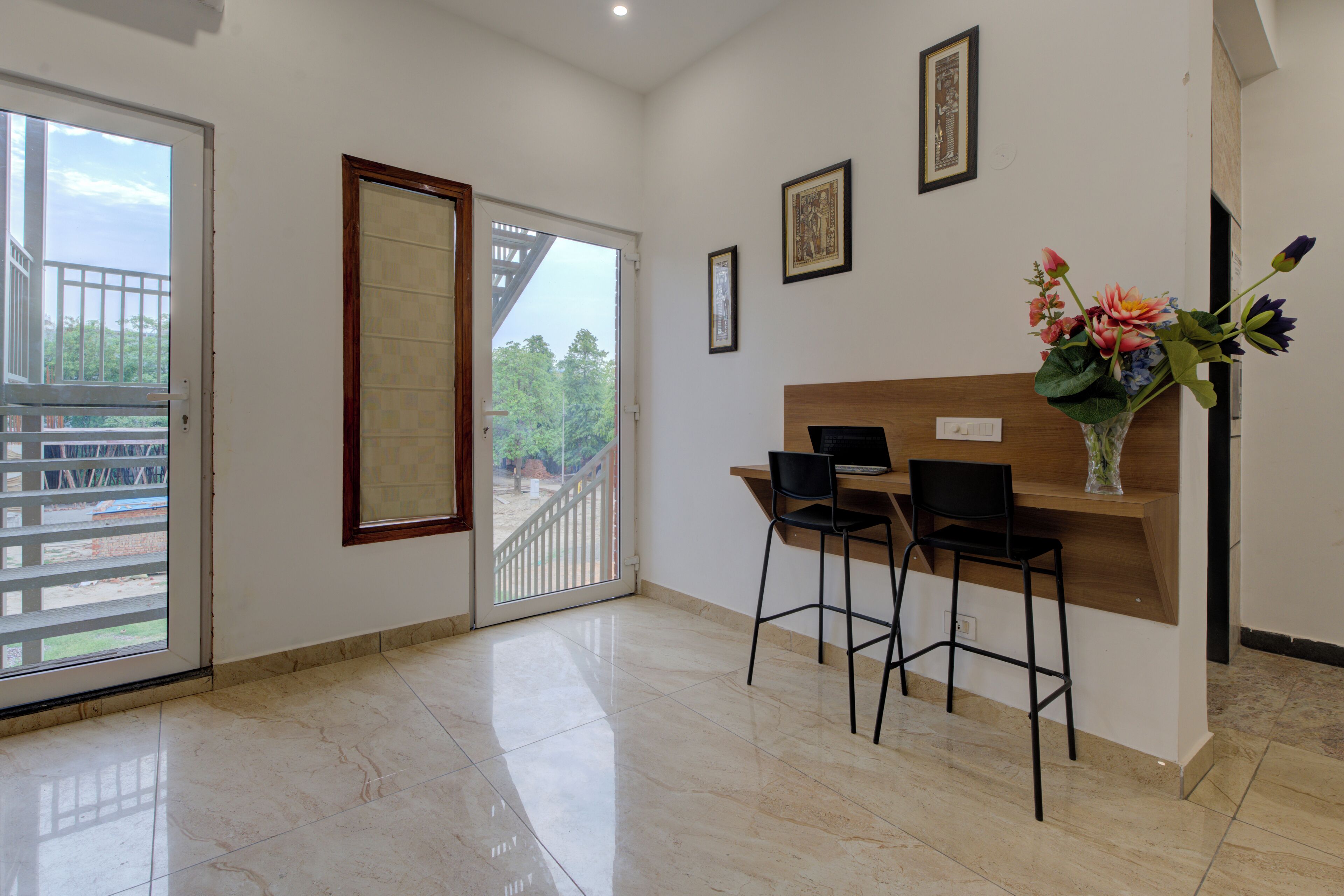 A room with a sliding glass door leading to an outdoor area, a wooden desk with two chairs, and a vase with flowers on the wall.