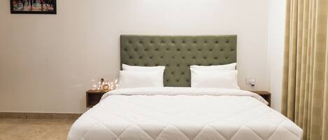 A neatly made bed with a tufted headboard, white bedding, and a nightstand with a lamp.