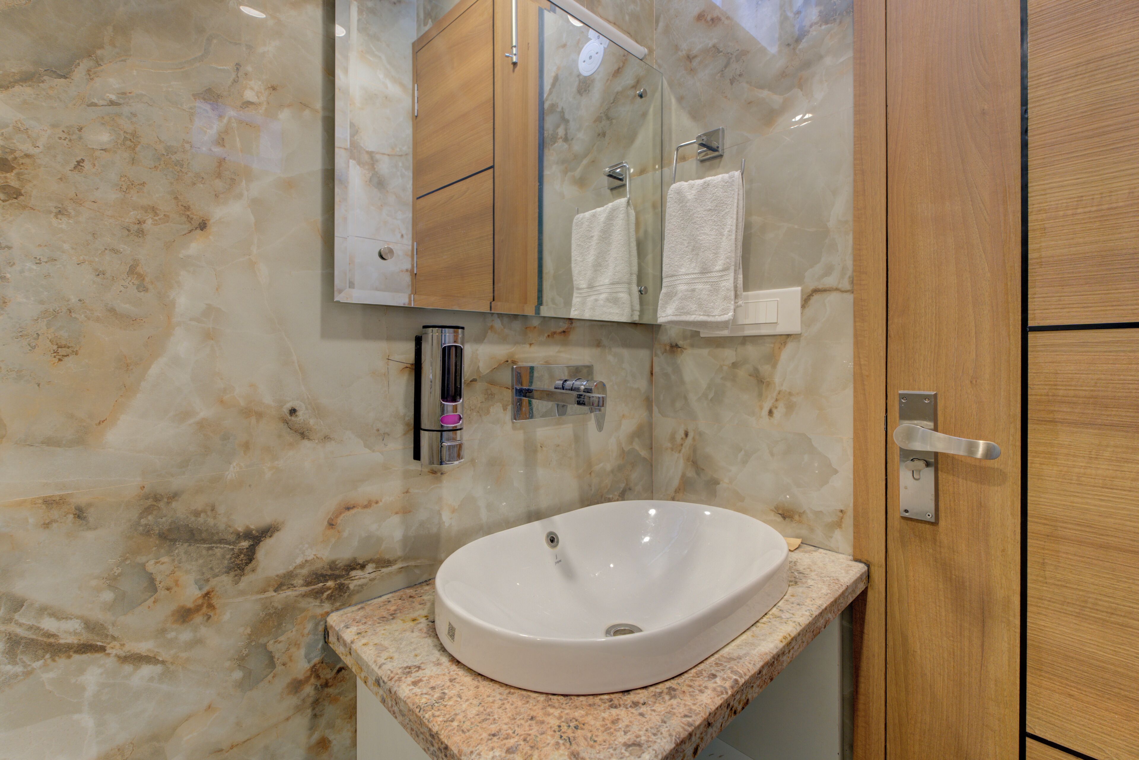 A bathroom with a marble wall, a white sink, and a wooden door.
