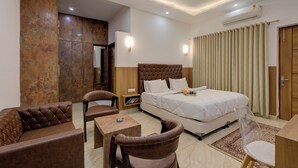 A hotel room with a large bed, a sofa, a chair, a small table, and a mirror. - Sandane Homes India Expo Centre & Mart (Greater Noida)