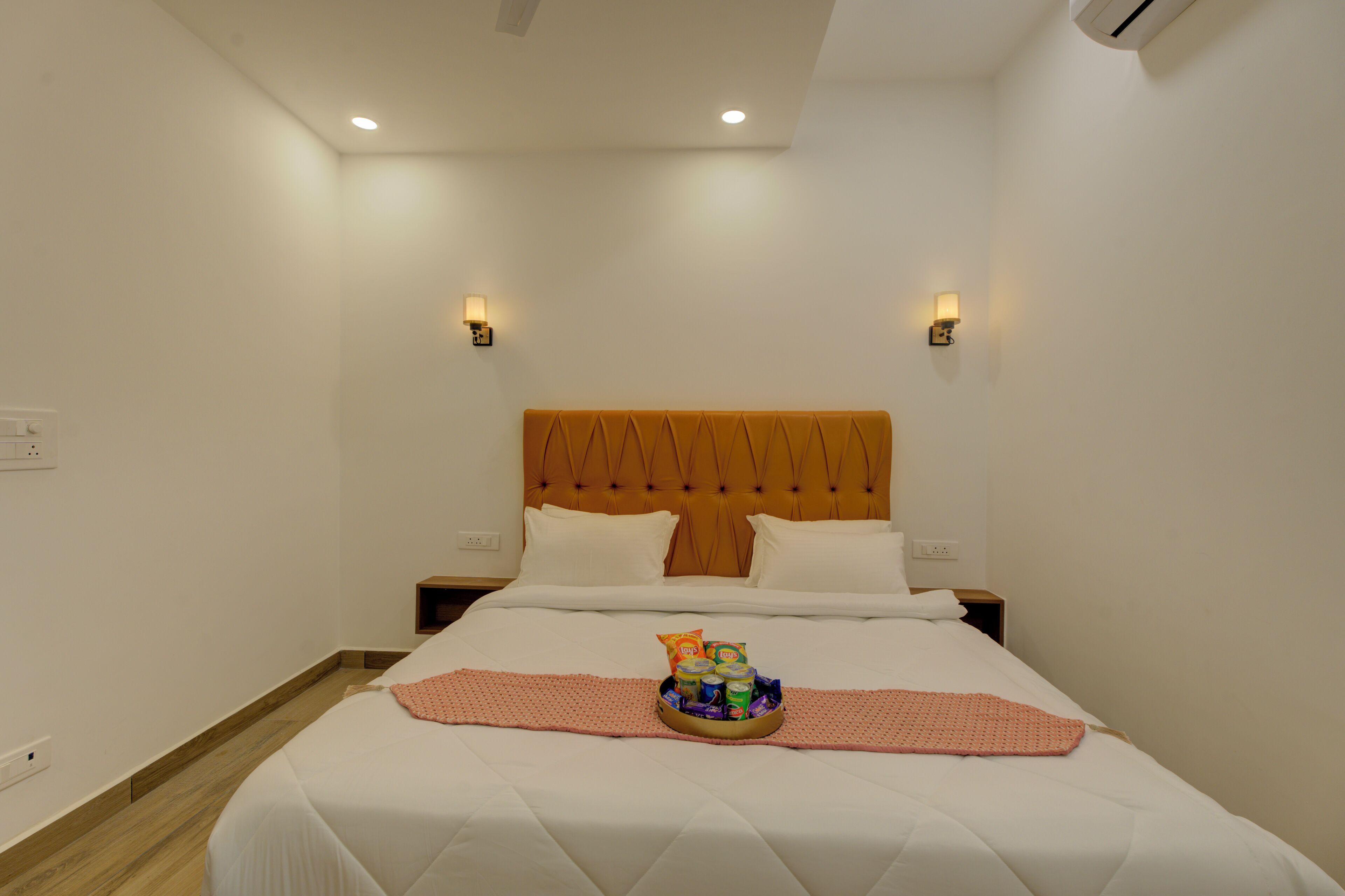 A hotel room with a bed, a headboard, two bedside tables, and a wall-mounted light fixture.