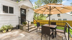 Een terras met een tafel, stoelen, een grote parasol en potplanten.