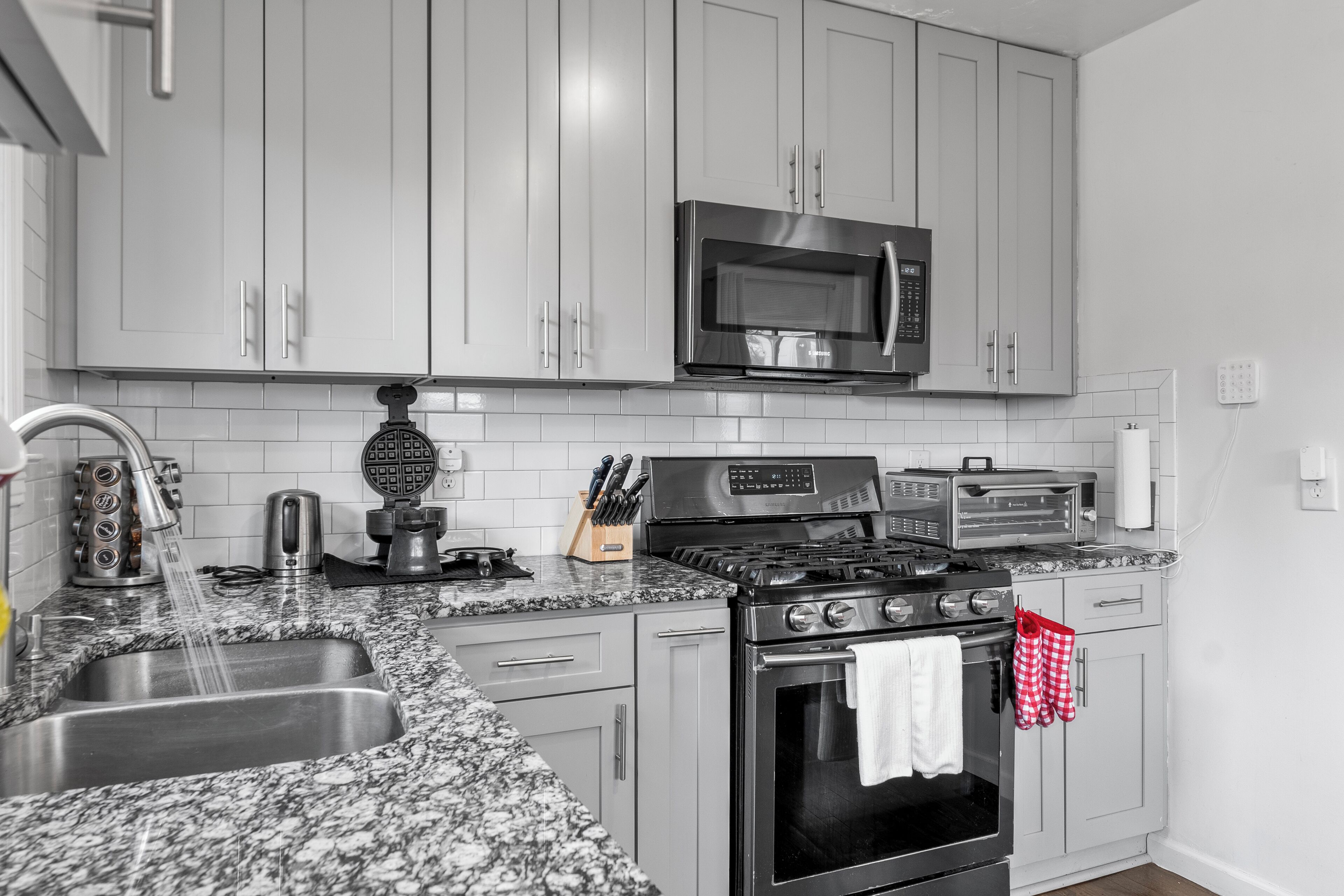 A modern kitchen with grey cabinets, a stainless steel sink, a microwave, a stove, and a toaster.