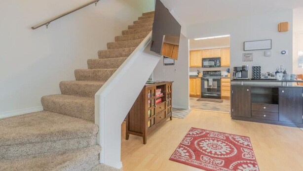 Eine Treppe führt zu einer zweiten Etage, ein Küchenbereich mit dunklen Schränken und ein Teppich mit rotem Muster auf dem Boden.