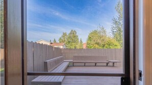 Eine Holzterrasse mit Bänken und Blick auf einen Garten mit Holzzaun und Bäumen.