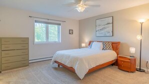 Ein Schlafzimmer mit Bett, Kommode, Deckenventilator, Fenster und Stehlampe.