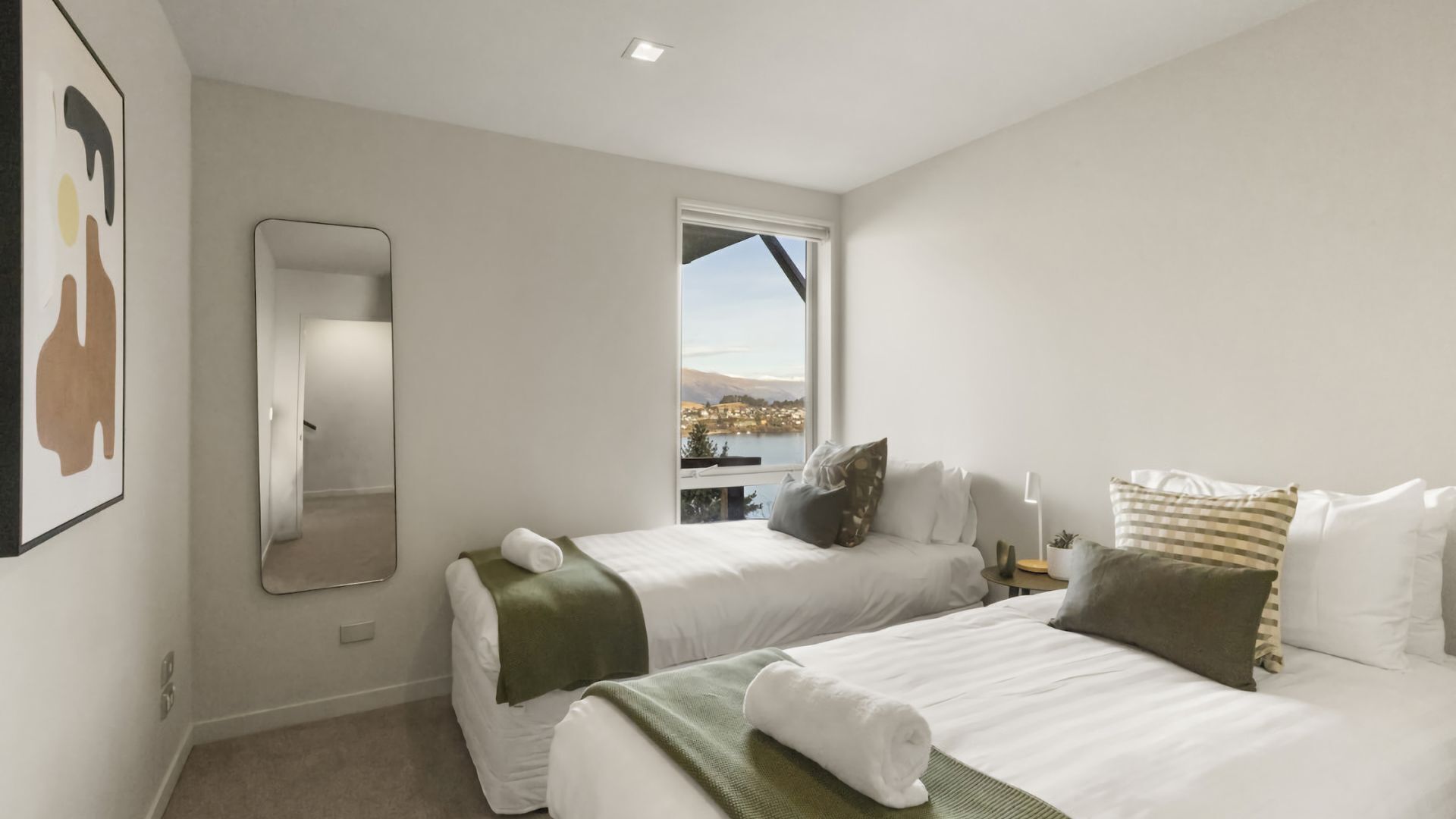 A modern hotel room with two beds, a large mirror, and a window offering a scenic view.