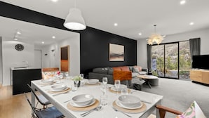 Uma sala moderna com área de jantar, uma parede de destaque preta, uma janela grande com vista e uma TV de tela plana.
