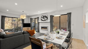 Uma sala de estar moderna com sofá, mesa de jantar posta para quatro pessoas e lareira.
