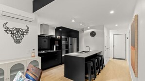 Cozinha moderna com armários pretos, uma ilha central com banquetas, uma obra de arte com tema de vaca e um relógio na parede.