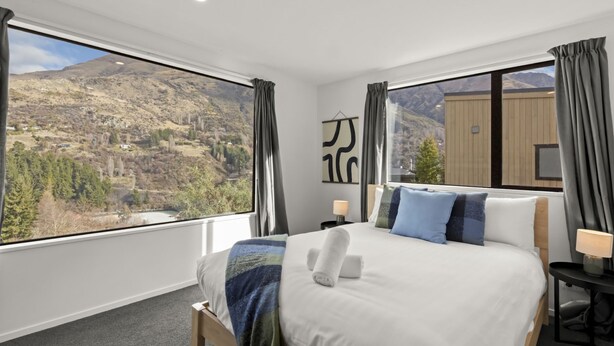 Quarto com cama grande, vista para montanhas e janela com cortinas.