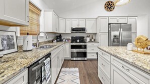 A modern kitchen with white cabinets, granite countertops, stainless steel appliances, and decorative lighting.